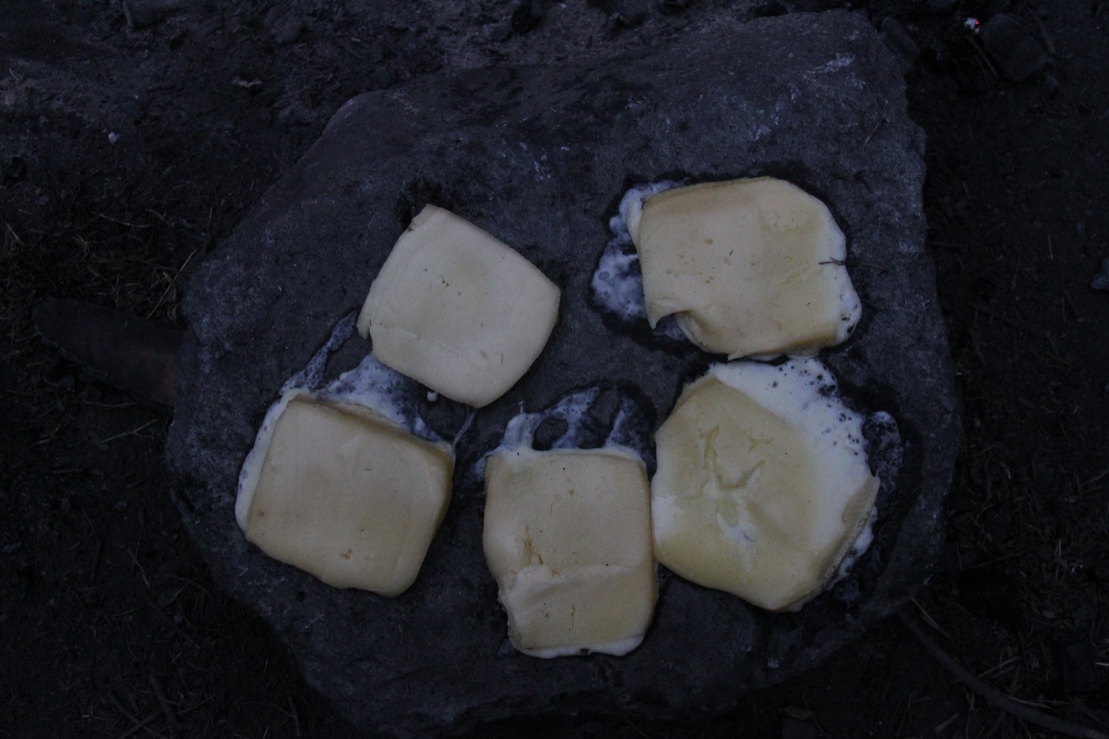Traditionelles Schweizer Raclette-Rezept — halbes Käserad schmilzt am offenen Feuer