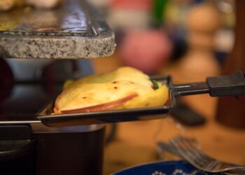 Traditional Swiss raclette recipe — half-wheel of raclette cheese melting by the fire with potatoes and charcuterie