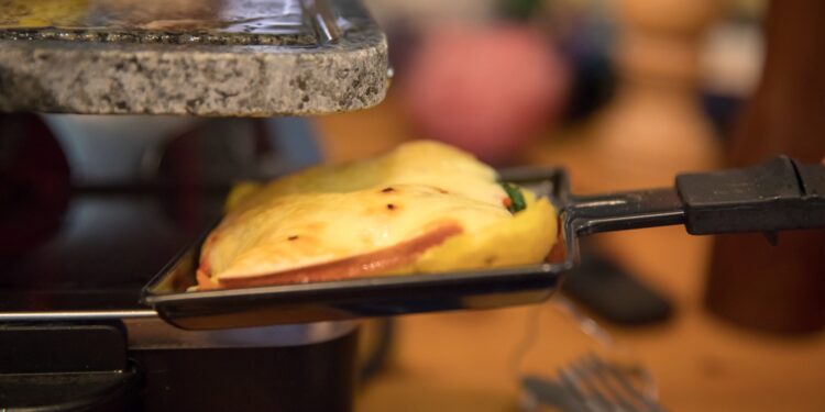 Traditional Swiss raclette recipe — half-wheel of raclette cheese melting by the fire with potatoes and charcuterie